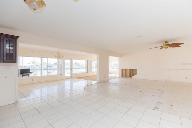 tiled empty room with ceiling fan with notable chandelier and a water view