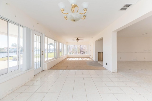 unfurnished sunroom with ceiling fan with notable chandelier and a water view