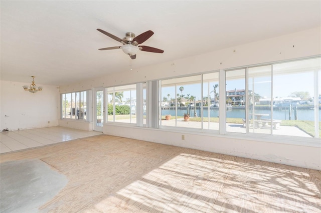 unfurnished sunroom with ceiling fan with notable chandelier and a water view