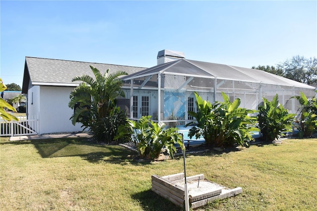 rear view of property featuring glass enclosure and a lawn