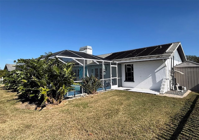 back of house with a lanai, a lawn, a storage shed, and solar panels