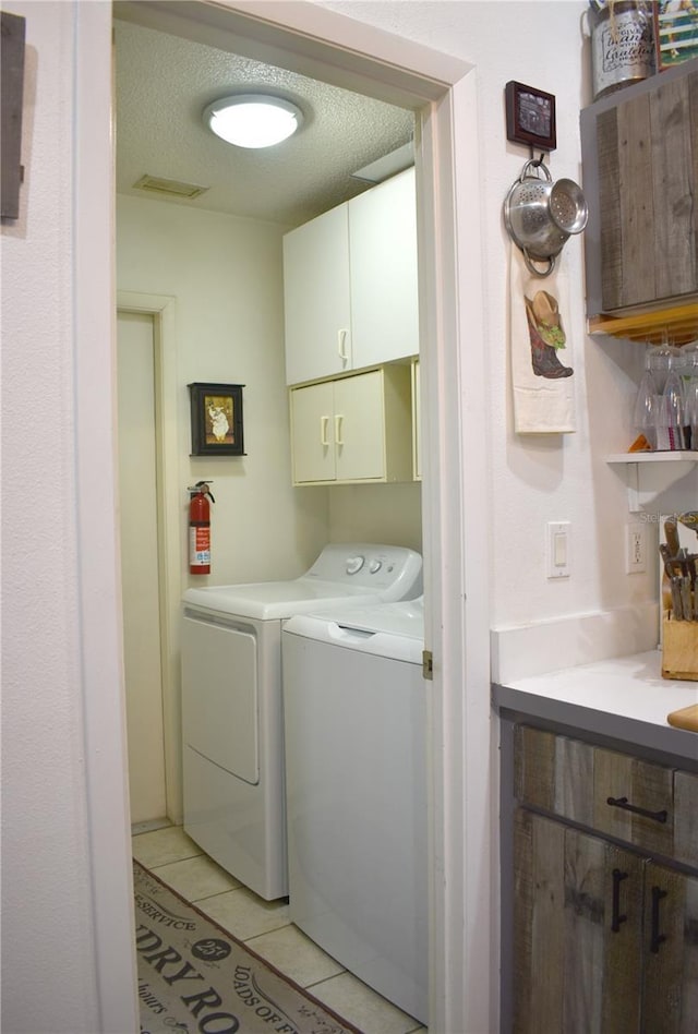 washroom with cabinets, light tile patterned floors, a textured ceiling, and washing machine and clothes dryer