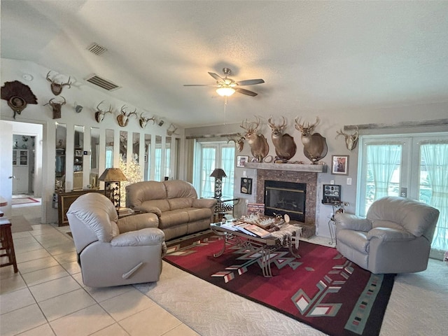 tiled living room featuring a textured ceiling, a premium fireplace, a wealth of natural light, and ceiling fan