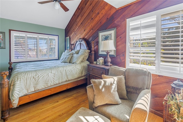 bedroom with ceiling fan, hardwood / wood-style floors, vaulted ceiling, and wooden walls