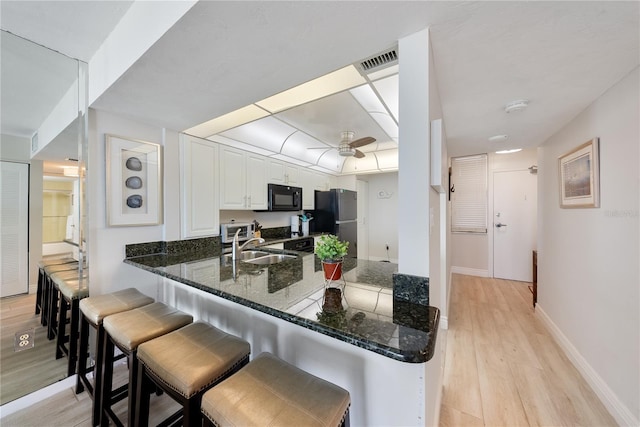 kitchen with kitchen peninsula, stainless steel fridge, sink, light hardwood / wood-style flooring, and white cabinetry