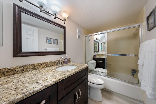 full bathroom with a textured ceiling, vanity, hardwood / wood-style flooring, enclosed tub / shower combo, and toilet