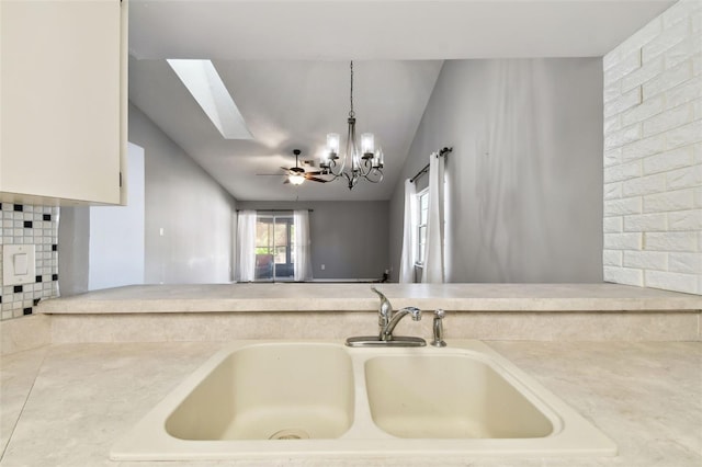 kitchen featuring tasteful backsplash, vaulted ceiling with skylight, ceiling fan with notable chandelier, sink, and pendant lighting