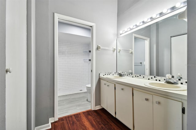 bathroom featuring toilet, wood-type flooring, vanity, and a tile shower