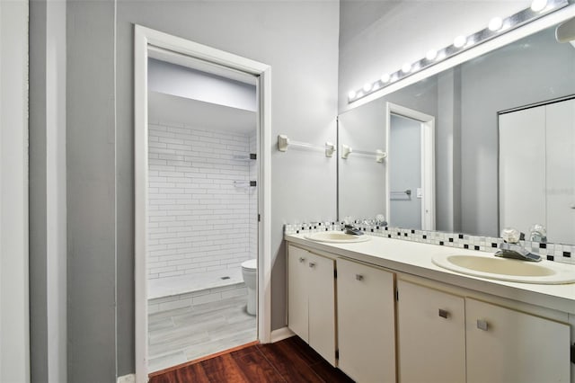 bathroom featuring hardwood / wood-style floors, vanity, toilet, and a tile shower