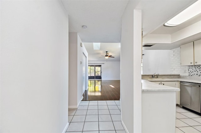 kitchen featuring light countertops, a sink, light tile patterned flooring, decorative backsplash, and dishwasher