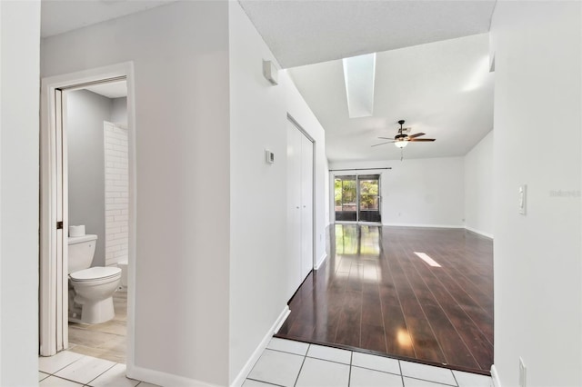 corridor featuring a skylight, baseboards, and tile patterned flooring