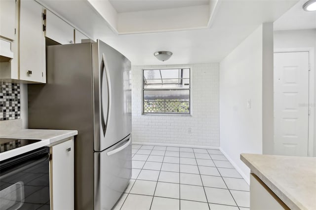 kitchen with light countertops, electric range oven, white cabinetry, and brick wall
