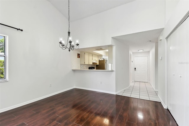 unfurnished dining area with a chandelier, high vaulted ceiling, wood finished floors, and baseboards