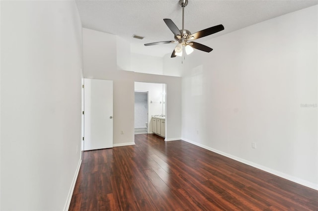 empty room with a textured ceiling, ceiling fan, baseboards, dark wood-style flooring, and visible vents