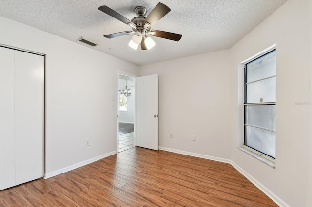unfurnished bedroom featuring baseboards, wood finished floors, visible vents, and a textured ceiling