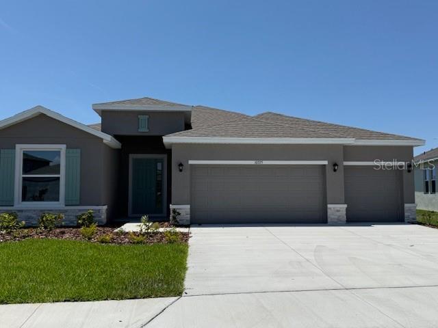 10725 Tippecanoe Pl, Parrish, FL 34219 - view of front facade with a garage, concrete driveway, stucco siding, a front lawn, and stone siding