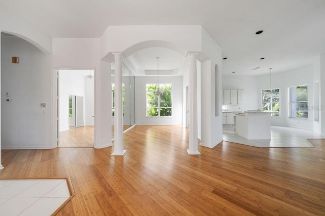 unfurnished living room featuring a tray ceiling, decorative columns, light hardwood / wood-style floors, and a notable chandelier