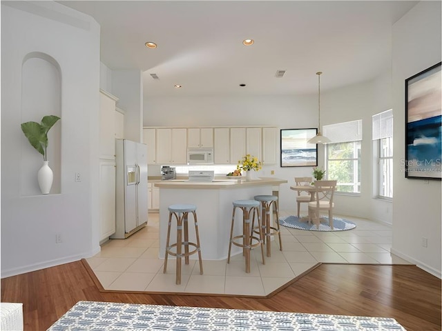 kitchen with a center island, a kitchen breakfast bar, pendant lighting, white appliances, and light tile patterned floors