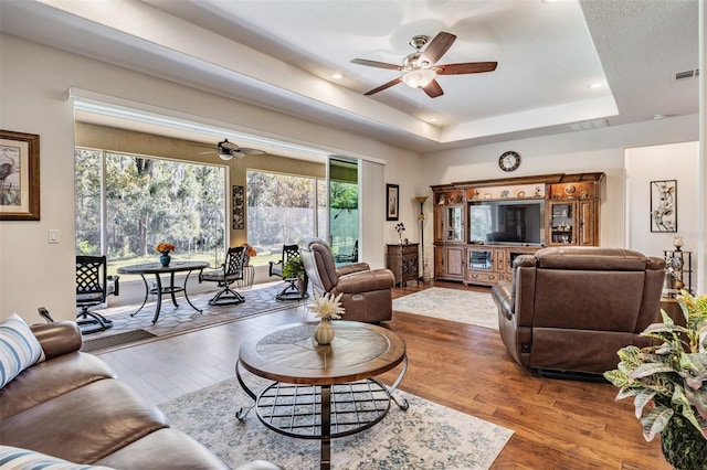 living room featuring hardwood / wood-style flooring, a raised ceiling, and ceiling fan