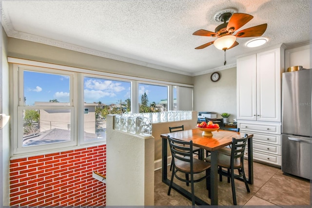 tiled dining space featuring ceiling fan, crown molding, a textured ceiling, and brick wall