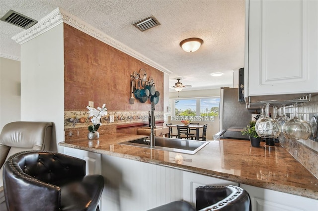 kitchen featuring stone counters, ceiling fan, a textured ceiling, a kitchen bar, and white cabinetry