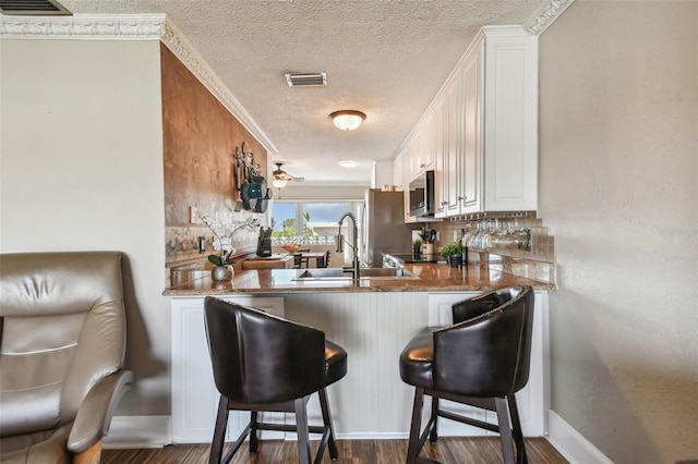 kitchen with decorative backsplash, dark hardwood / wood-style flooring, a breakfast bar, sink, and white cabinets