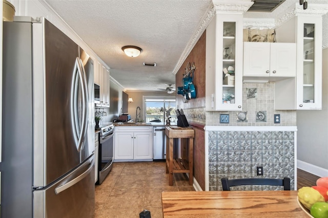 kitchen featuring white cabinets, ornamental molding, tasteful backsplash, kitchen peninsula, and stainless steel appliances