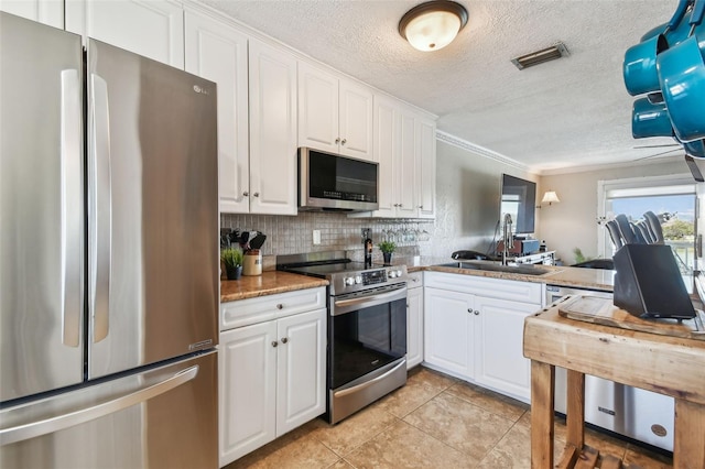 143 94th Ave Unit 2, Treasure Island, FL 33706 - kitchen featuring appliances with stainless steel finishes, a textured ceiling, ornamental molding, white cabinetry, and light tile patterned floors