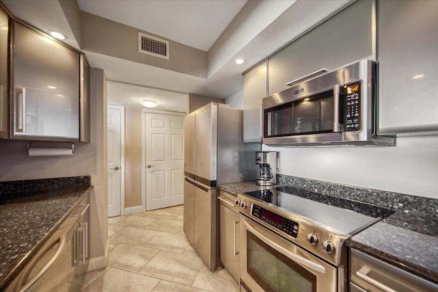 kitchen with light tile patterned floors, appliances with stainless steel finishes, and dark stone counters