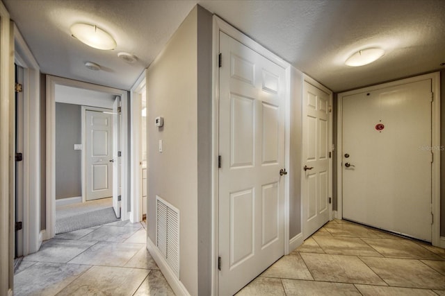 hallway with a textured ceiling and light tile patterned flooring