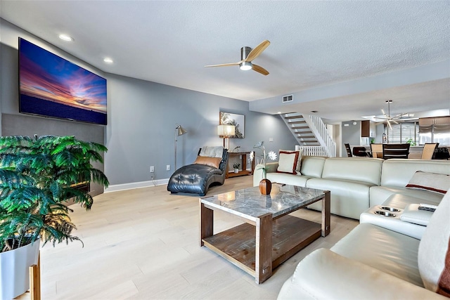 living room with ceiling fan, a textured ceiling, and light wood-type flooring