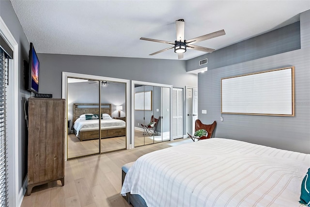 bedroom with lofted ceiling, two closets, ceiling fan, light wood-type flooring, and a textured ceiling