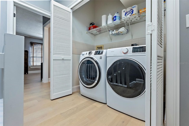 clothes washing area featuring a textured ceiling, light wood-type flooring, and washer and clothes dryer