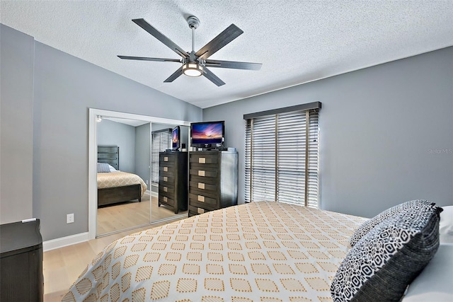 bedroom featuring ceiling fan, light hardwood / wood-style floors, a textured ceiling, lofted ceiling, and a closet