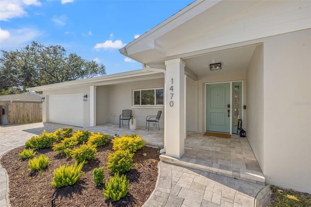 property entrance featuring an attached garage, driveway, fence, and stucco siding