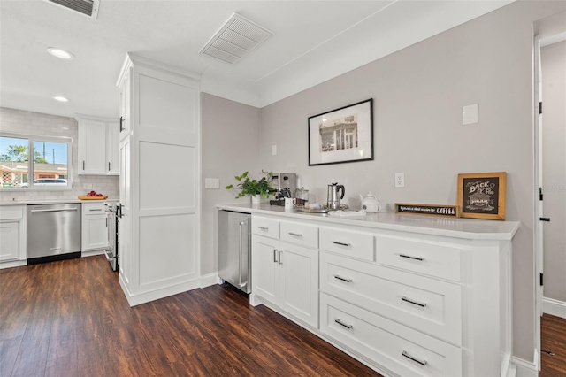 kitchen with kitchen peninsula, appliances with stainless steel finishes, backsplash, dark wood-type flooring, and white cabinets