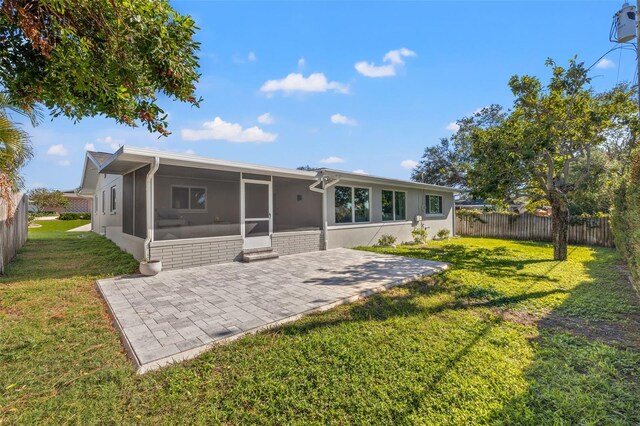 rear view of house with a sunroom, a patio area, and a lawn