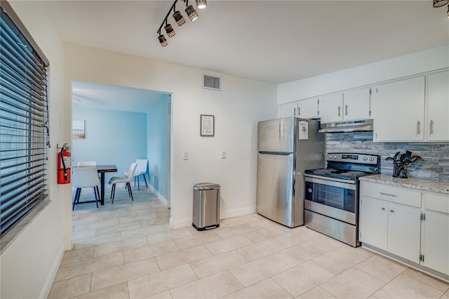 kitchen with light stone countertops, stainless steel appliances, light tile patterned floors, backsplash, and white cabinets