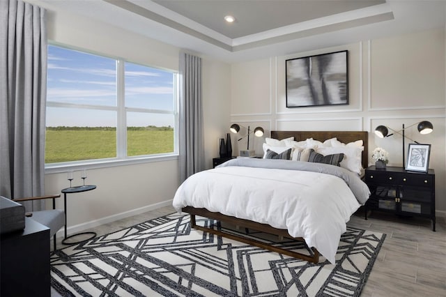 bedroom with light wood-type flooring and a tray ceiling