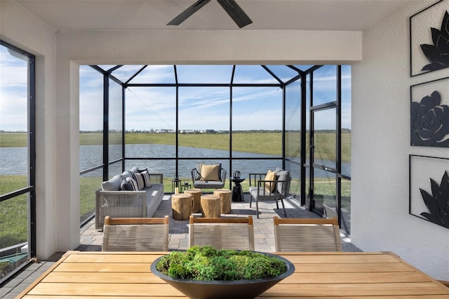 sunroom with ceiling fan and a water view