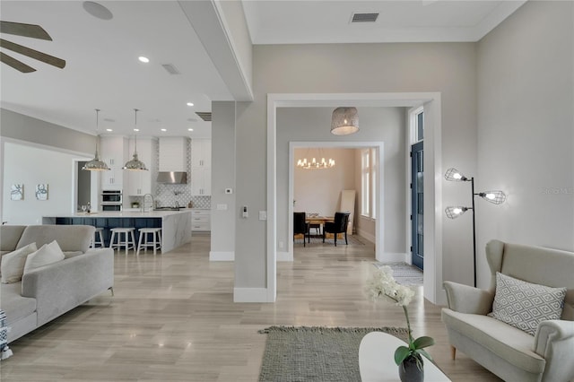 living room with ceiling fan with notable chandelier, sink, and light hardwood / wood-style flooring