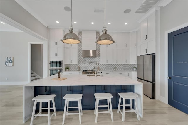 kitchen with white cabinetry, hanging light fixtures, light stone counters, a kitchen island with sink, and appliances with stainless steel finishes