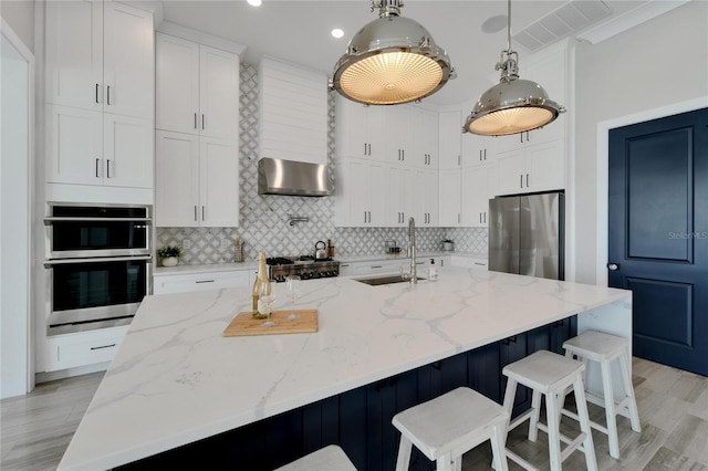 kitchen with white cabinets, appliances with stainless steel finishes, a kitchen island with sink, and sink