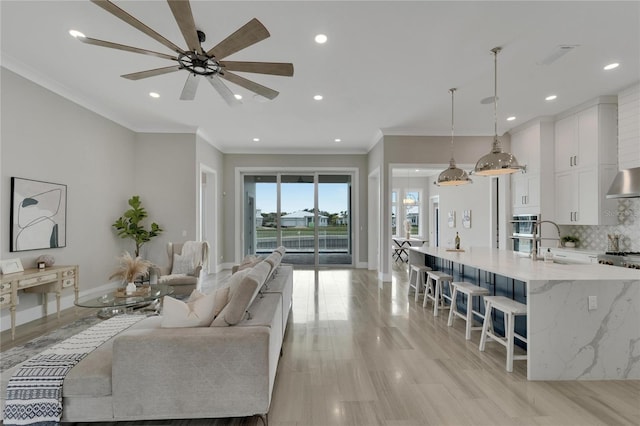 living room featuring ceiling fan, sink, crown molding, and light hardwood / wood-style flooring