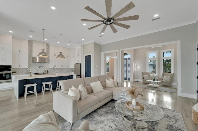 living room with ceiling fan, sink, light wood-type flooring, and crown molding