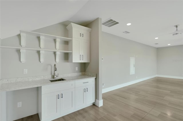 kitchen featuring white cabinetry, sink, ceiling fan, light stone counters, and light wood-type flooring