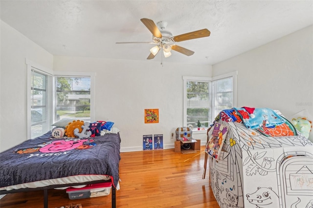 bedroom with ceiling fan, wood-type flooring, and multiple windows