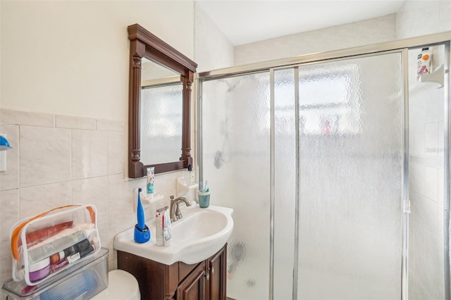 bathroom featuring vanity, toilet, a shower with door, and tile walls