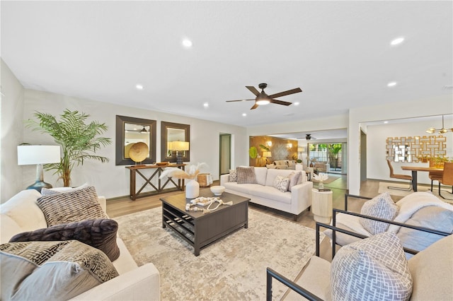 living room with ceiling fan with notable chandelier and light wood-type flooring