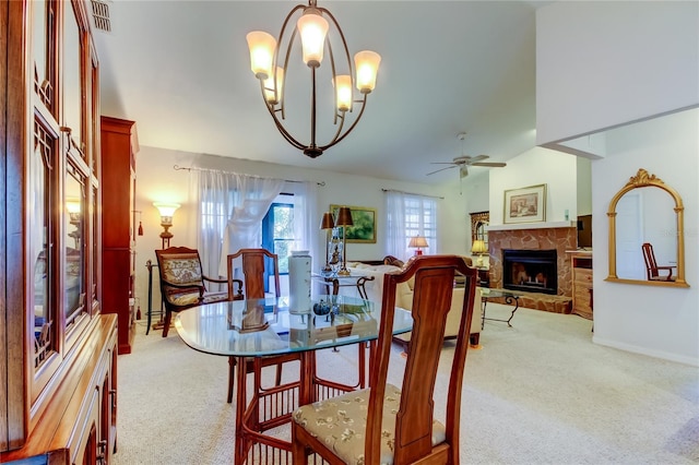 carpeted dining space with a stone fireplace and ceiling fan with notable chandelier